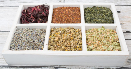 Dried herbal tea leaves, lavender, rooibos, chamomile, linden flower, hibiscus, Japanese green white box over wooden background