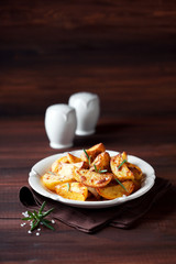 Roasted potato wedges with rosemary on plate, selective focus
