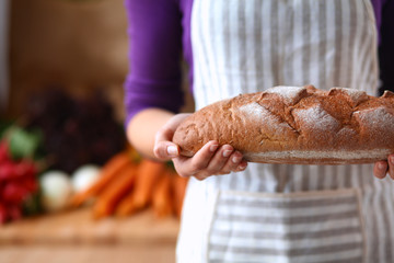 Young woman holding tasty fresh bread in her kitchen