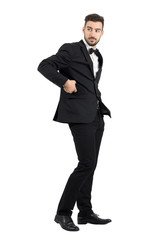 Obraz na płótnie Canvas Side view of confident handsome man in tuxedo putting cellphone in coat pocket turning behind. Full body length portrait isolated over white studio background. 