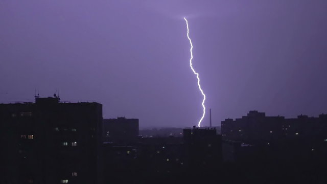 Large wide lightning bolt strikes night city, sounds of rain and thunder. Time-lapse of natural disaster raging over dark residential area in town. Stormy weather forecast. Dramatic events in country