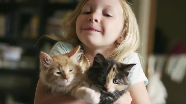 A little girl hugging two kittens in her arms