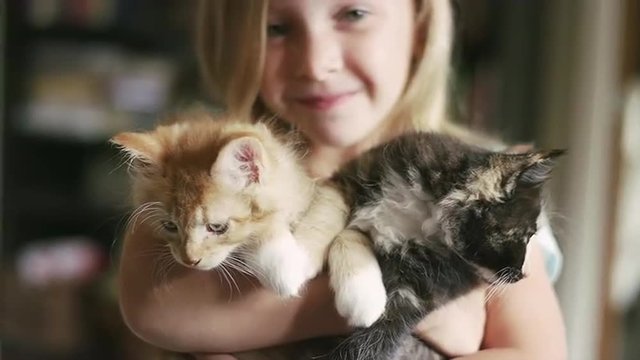 A little girl smiling and holding two kittens in her arms
