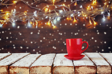 Obraz na płótnie Canvas Cup of hot coffee on wooden table in front of garland lights background 