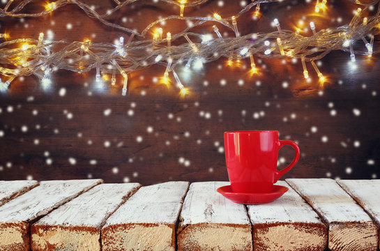 Cup of hot coffee on wooden table in front of garland lights background
