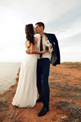 beautiful groom and bride in wedding clothes posing on sea coast - 97494471
