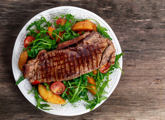 rare beef steak with roasted potatoes, tomatoes and wild rocket leaves. on old wooden table