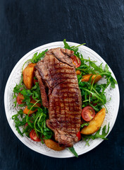 rare beef steak with roasted potatoes, tomatoes and wild rocket leaves. on old blue stone background