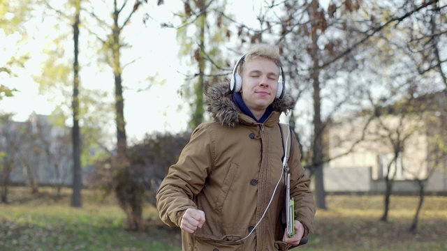 Boy listening music on headphones and dancing in the autumnal park
