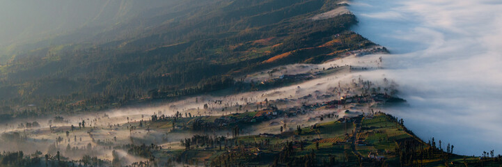 Mist and fog of smoking Volcano Bromo entering a Field and city