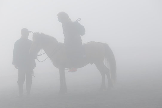 Fototapeta Silhouette of two person and horse in fog and smoke of volcano Bromo