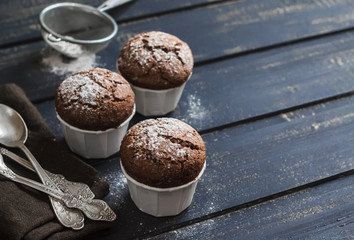 Delicious vegan chocolate muffins with icing sugar on dark wooden surface