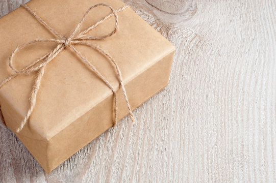Gift box packed into brown paper and twine on old white wooden table with space for text