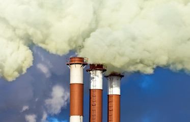 Industrial chimneys with smoke over blue sky