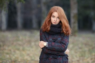 Outdoors portrait of young beautiful redhead woman in scarf and jacket on forest blurred background