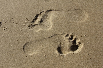 Fototapeta na wymiar feet steps in sandy beach, jing and jang