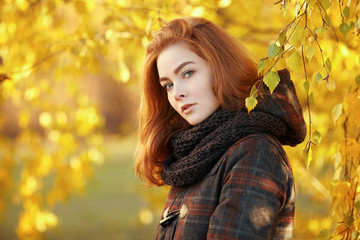 Outdoors portrait of young beautiful redhead woman in scarf and jacket on yellow autumn foliage background