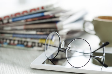 Stack of newspapers, eyeglasses and digital tablet