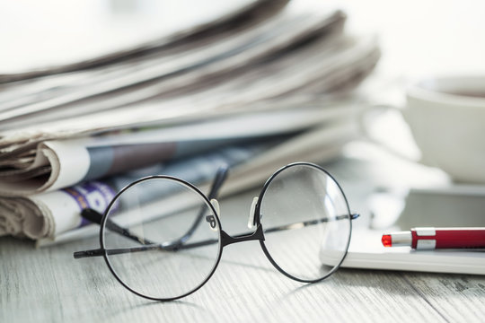 Stack of newspapers, eyeglasses on table