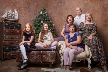 Obraz na płótnie Canvas Большая семья с бабушкой, дедушкой, мамами и девочками сидят около новогодней елки