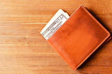 Dollars in brown wallet on wooden table