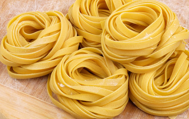 Italian homemade raw rolled fettuccine pasta with flour on wooden cutting board.