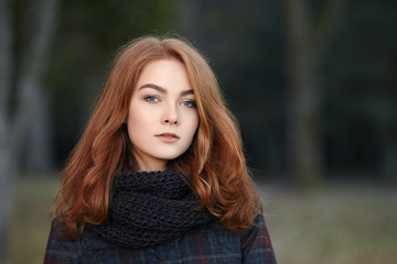 Art portrait of young elegant redhead woman  in scarf and plaid jacket with blurred forest background outdoors