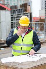 Construction worker with yellow hardhat and safety jacket checking blueprint