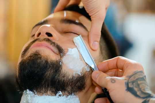 Professional barber shaving the beard of his client 