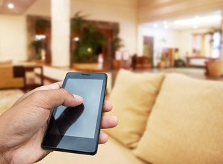 Hand hold and touch screen smart phone, tablet,cellphone on blur image of modern living room at home.