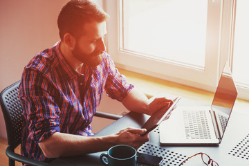 bearded man working with laptop and digital tablet in morning su