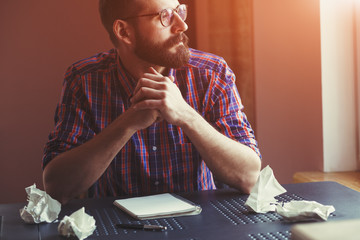 Bearded man sitting near blank copy book and thinking