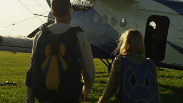 Man and Girl with Parachutes Moving towards the Plane. Shot on RED Cinema Camera.
