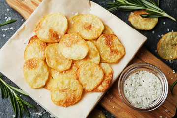 Homemade potato chips with sea salt and herb on wooden cutting board, top view