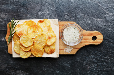 Homemade potato chips with sea salt and herb on wooden cutting board, top view