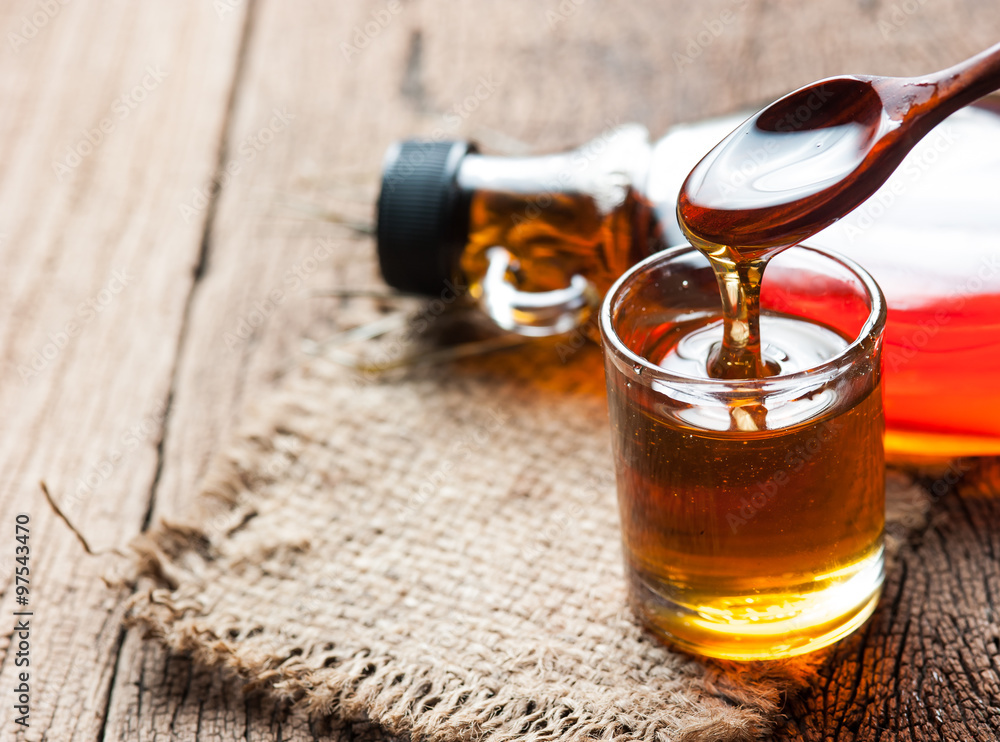 Wall mural maple syrup in glass bottle on wooden table