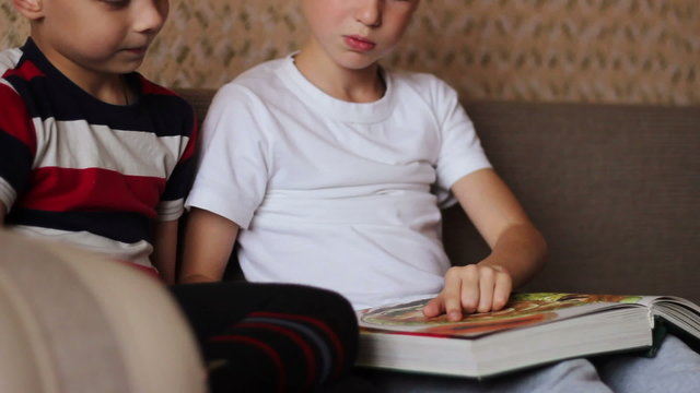 Two boys sitting on a couch  and read a book smiling