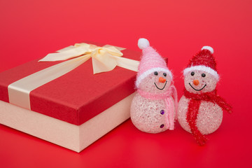 two smiling toy christmas snowman and a present box on red background