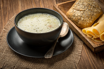 Cheese soup in a black plate on the rustic wooden background.