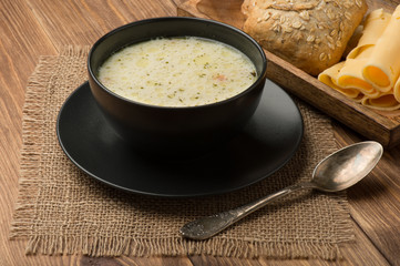 Cheese soup in a black plate on the rustic wooden background.