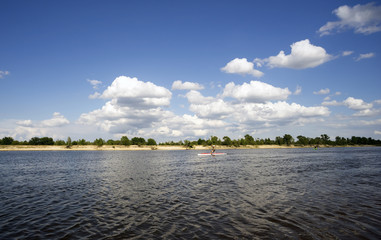 Summer landscape with river and clouds.The man practicing in rowing on a kayak.