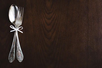 Fork and spoon tied with white ribbon on wooden table.