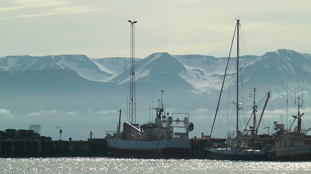 ships in harbor of husavik in front of scenic mountain range in iceland