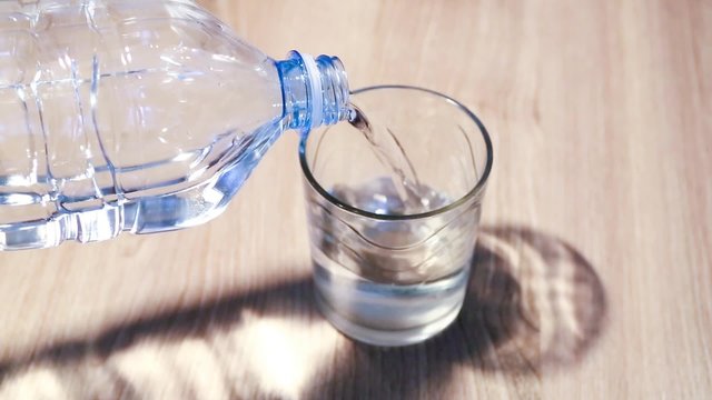 bottiglia di plastica trasparente versa bevanda acqua nel bicchiere sul tavolo
