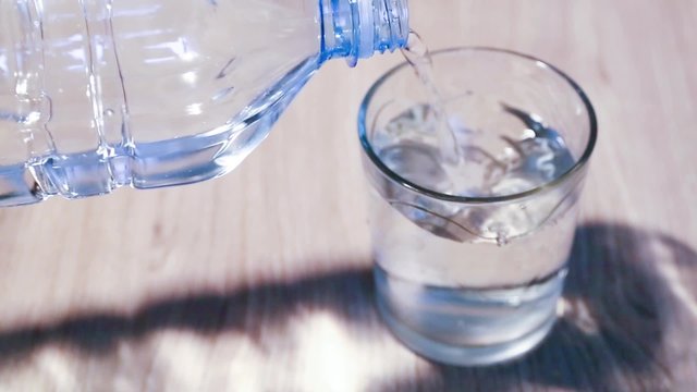 bottiglia di plastica trasparente versa bevanda acqua nel bicchiere sul tavolo
