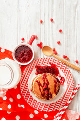
hearty breakfast, sweet American pancakes with raspberry , cherry or strawberry jam , berries and milk on a wooden background