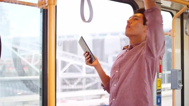 A young man standing on a bus and taking photos out the window with a tablet