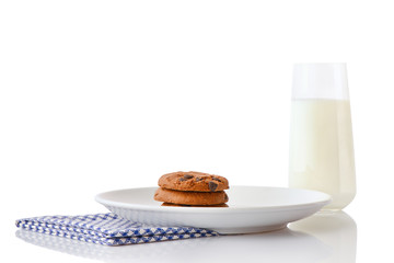 Stack of three homemade chocolate chip cookies on white ceramic plate on blue napkin and glass of milk, isolated on white background