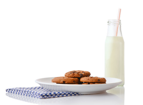 Pile of homemade chocolate chip cookies on white ceramic plate on blue napkin and bottle of milk with straw, isolated on white background