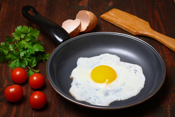 Pan of fried eggs, with cherry-tomatoes and parsley on a wooden table surface